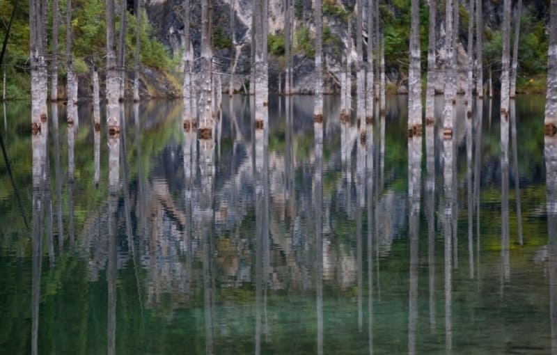 Редкое зеркальное отражение: гладь Каинды превращает лес призраков в двойной мир - над водой и под водой. Прозрачность озера позволяет увидеть затопленные деревья целиком, а отражённые скалы усиливают магический пейзаж.